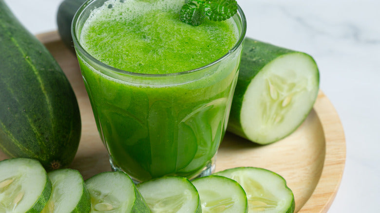 a glass of cucumber juice surrounded by cucumbers
