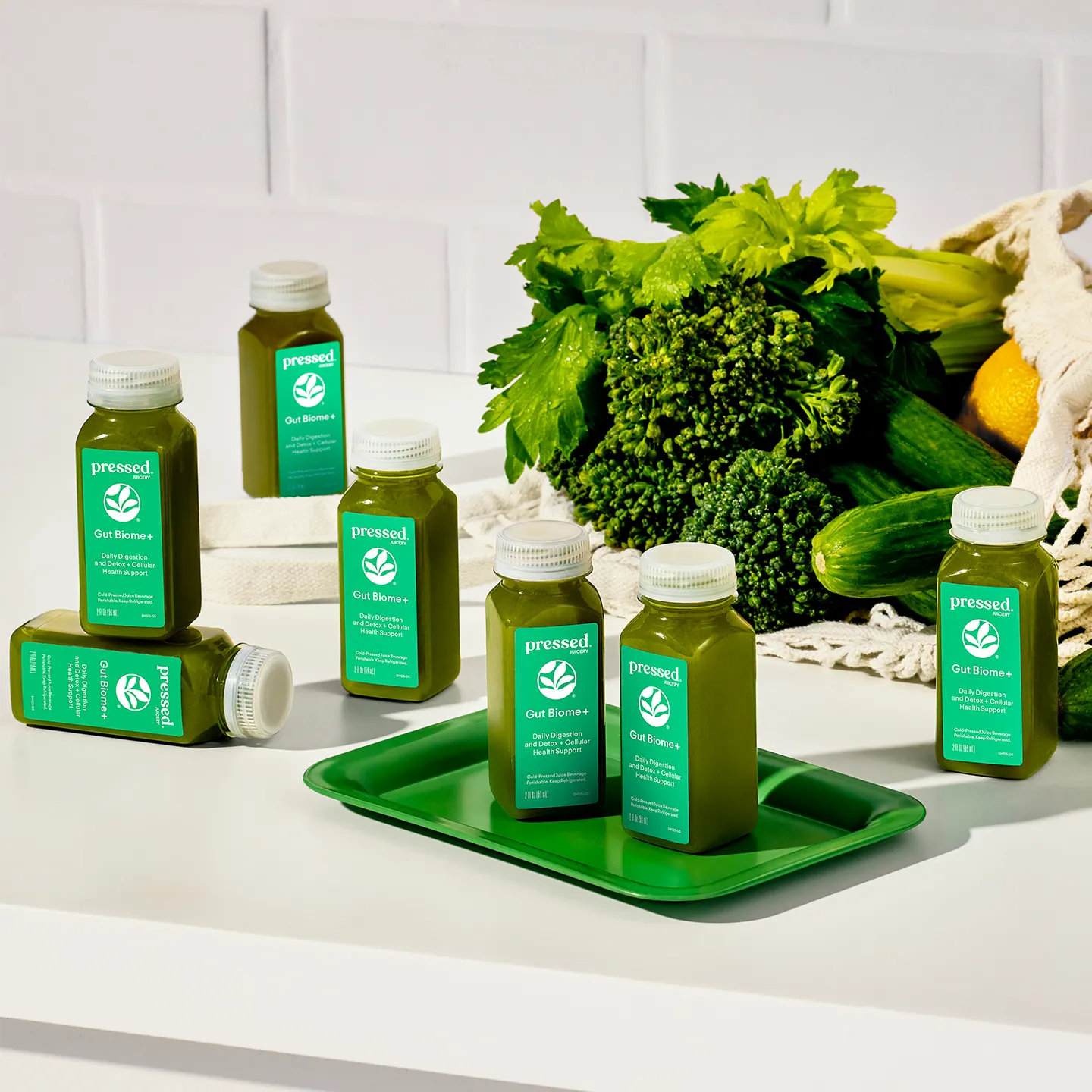Green juice bottles on a tray with fresh vegetables in the background