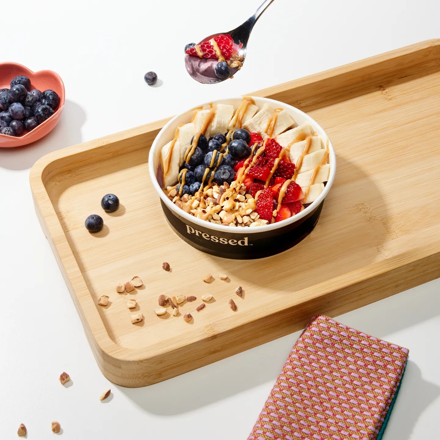 Fruit and yogurt bowl on a wooden tray with berries and a spoonful of the dessert.