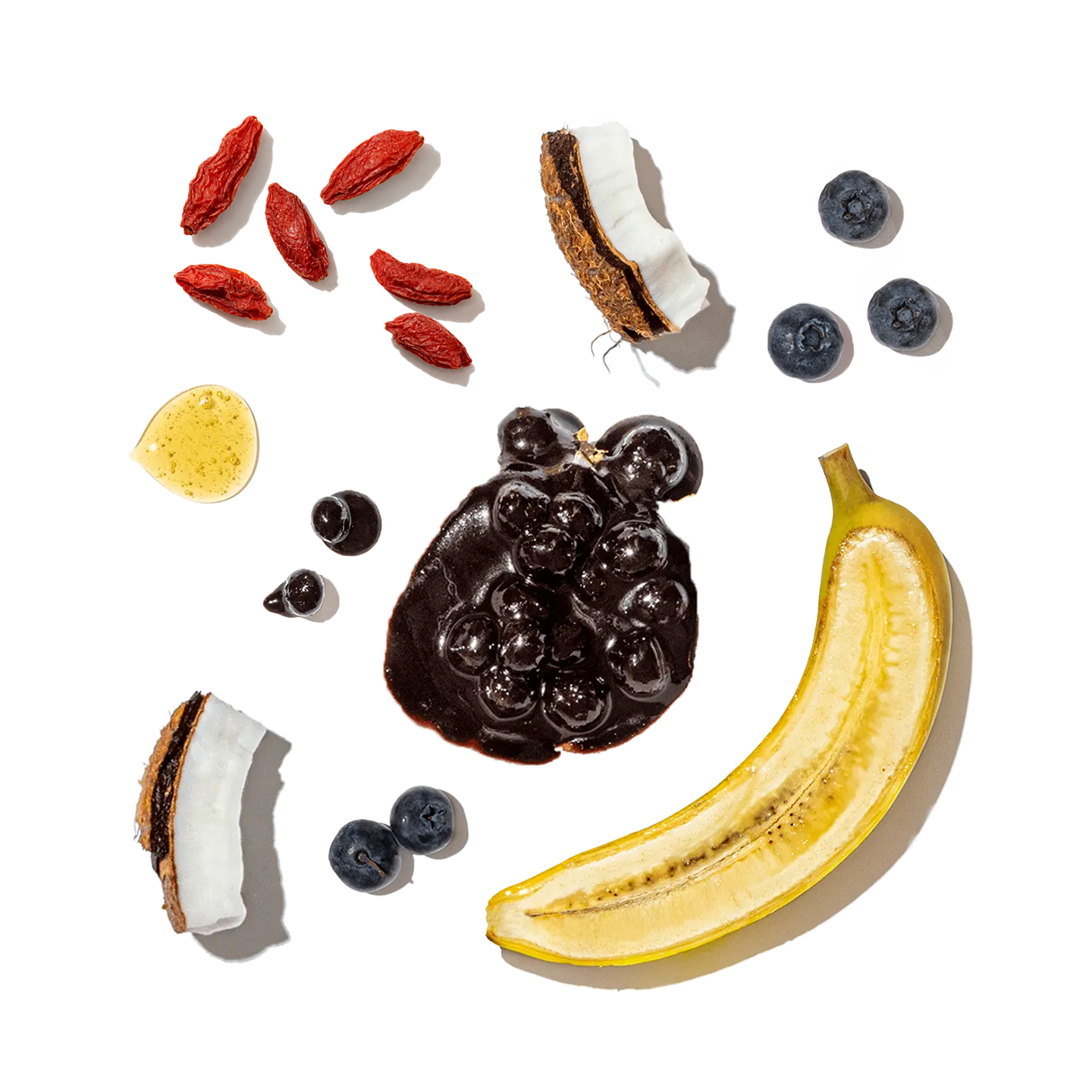 Fruits and ingredients including a banana, blueberries, goji berries, a coconut, and honey on a white background.