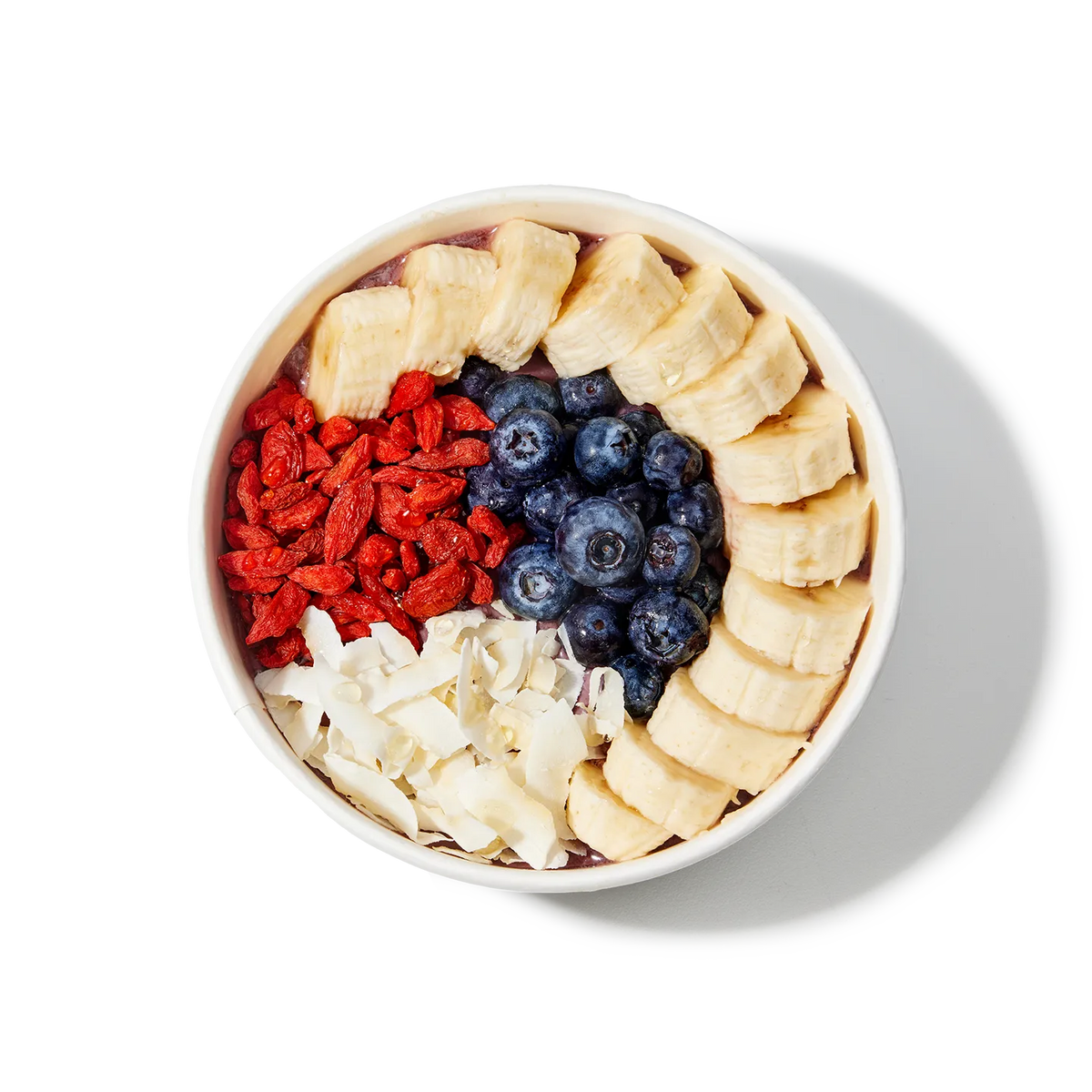 Fruit bowl with bananas, blueberries, goji berries, and coconut flakes on a white background