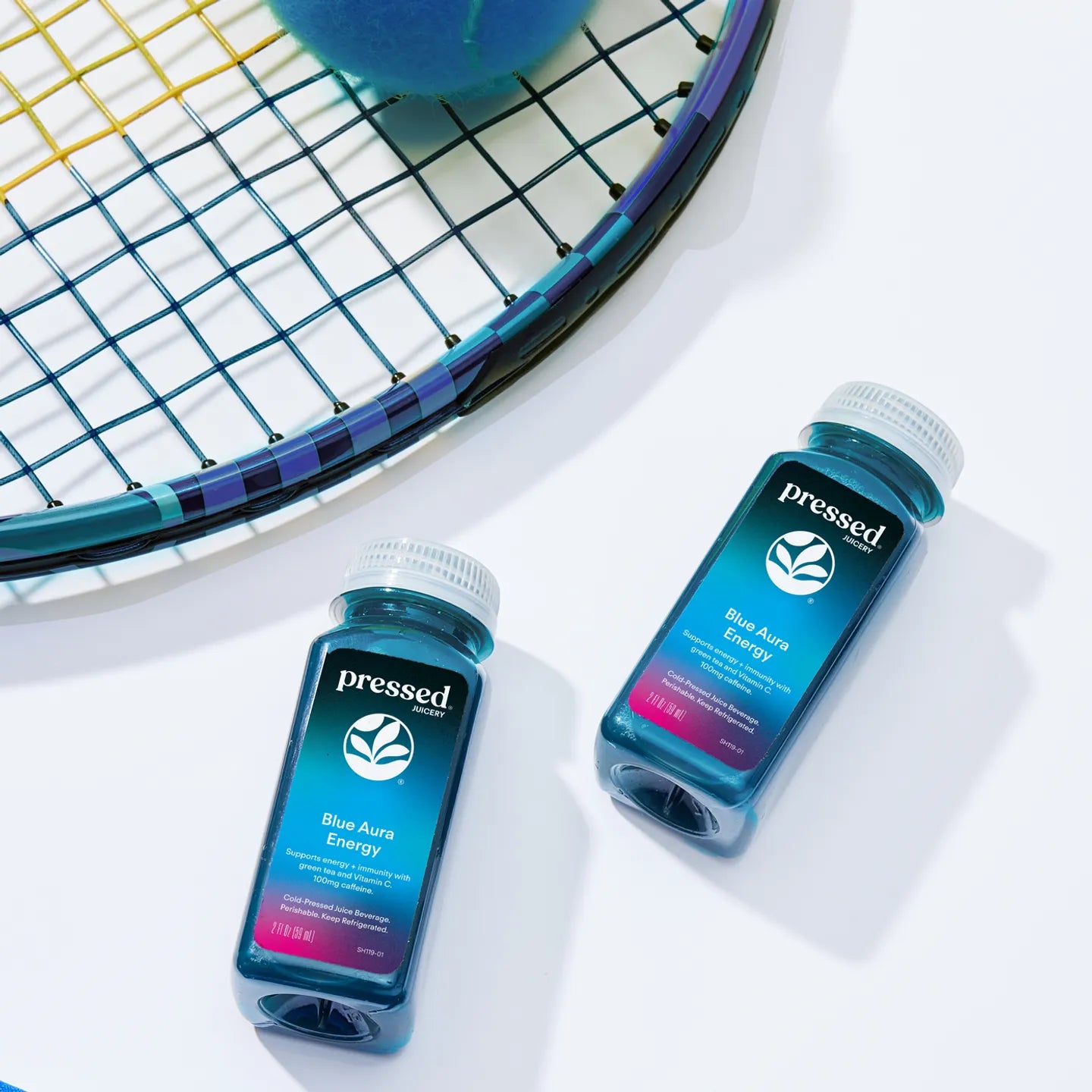 Two 'pressed' energy drink bottles on a white surface with a tennis racket in the background.