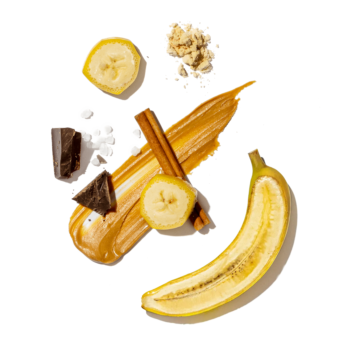 Ingredients including banana slices, almond butter, and a chocolate chunks with sea salt on a transparent background