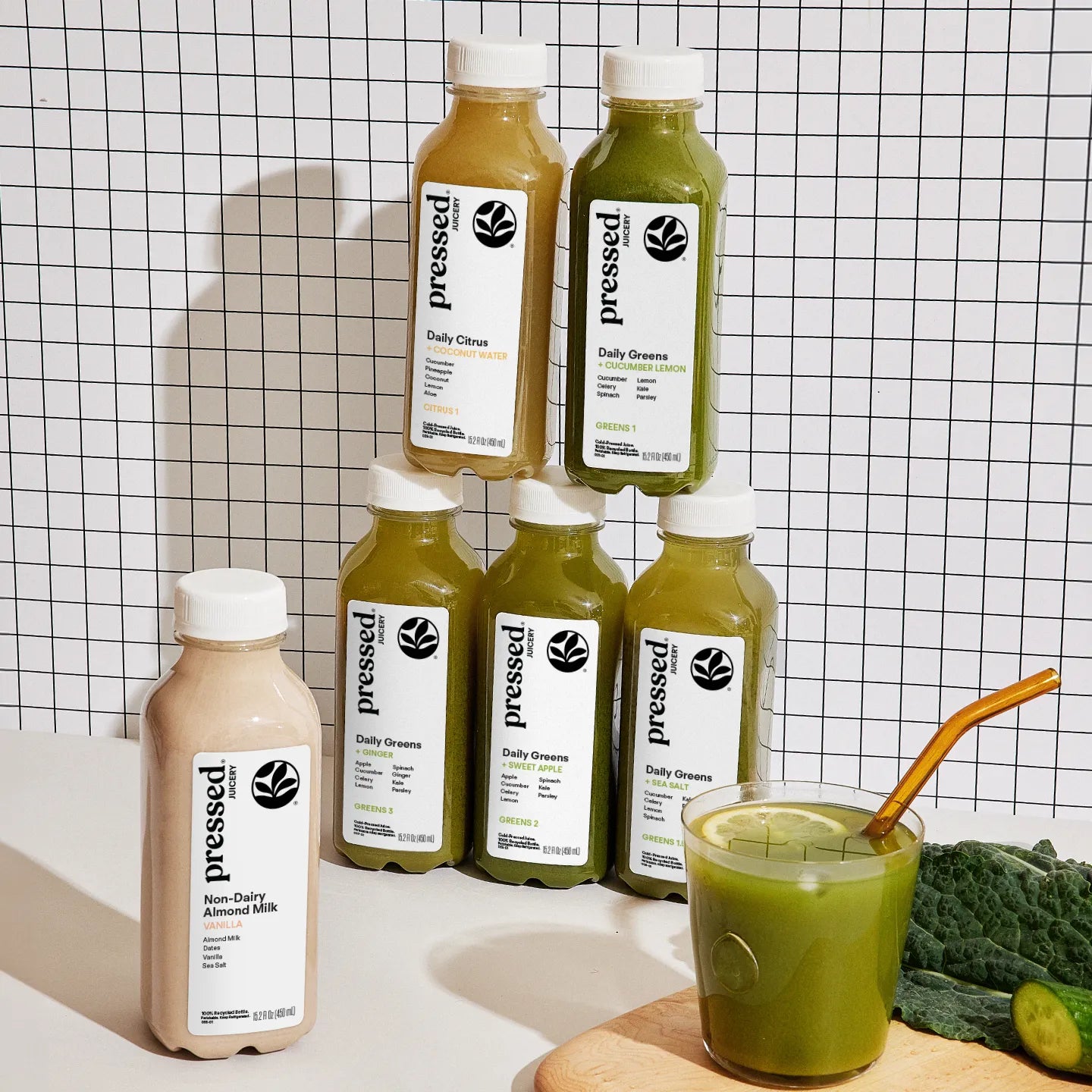 Bottles of 'pressed' brand juice on a checkered background with a glass of juice and ingredients.