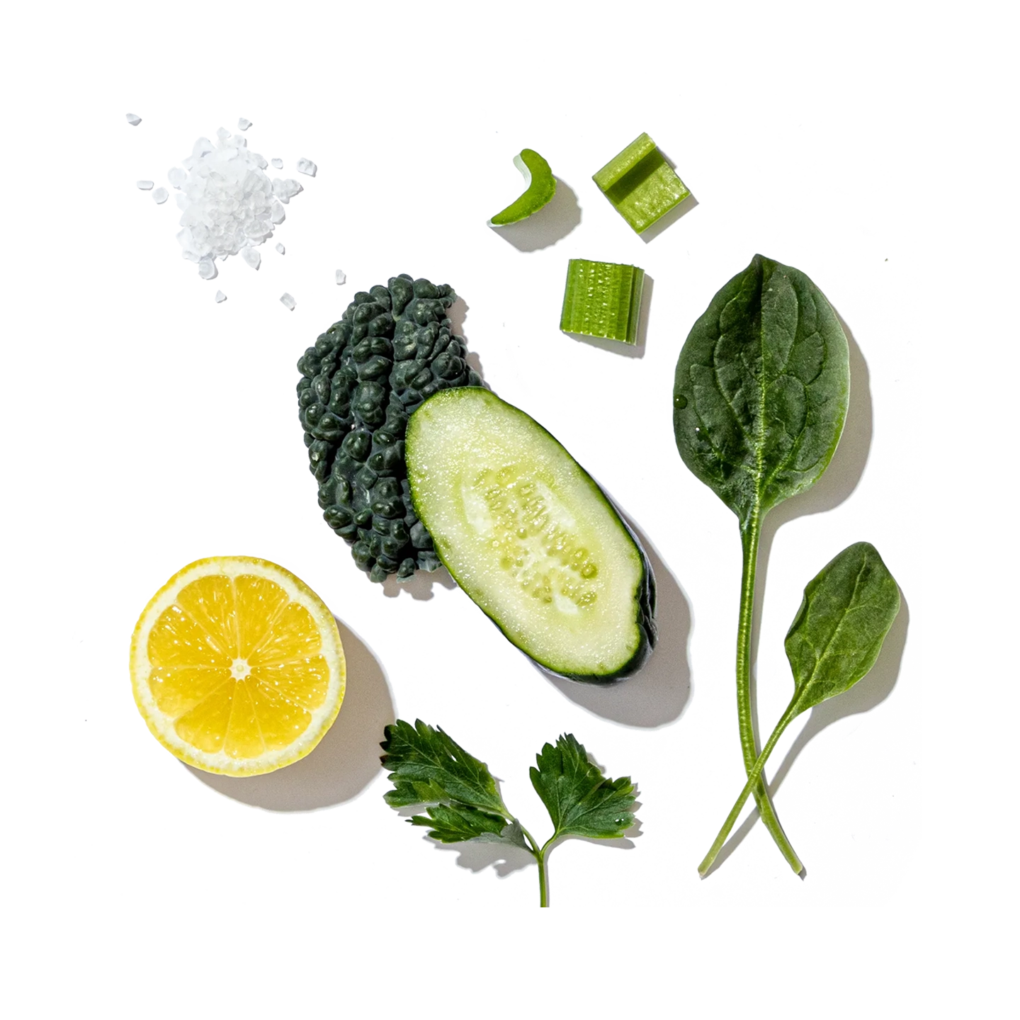 Various green vegetables and a lemon on a white background with black specks.