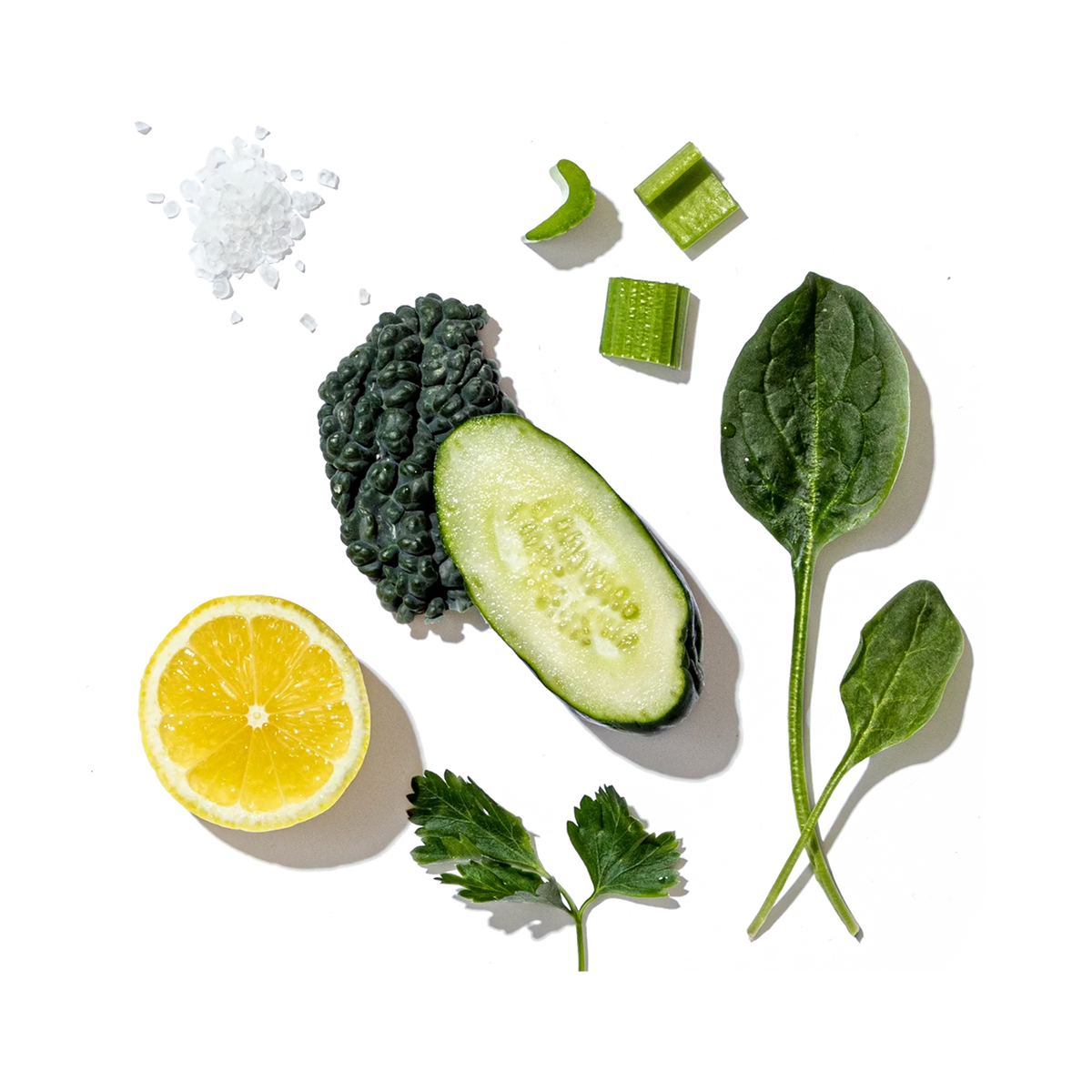 Various green vegetables and a lemon on a white background with black specks.
