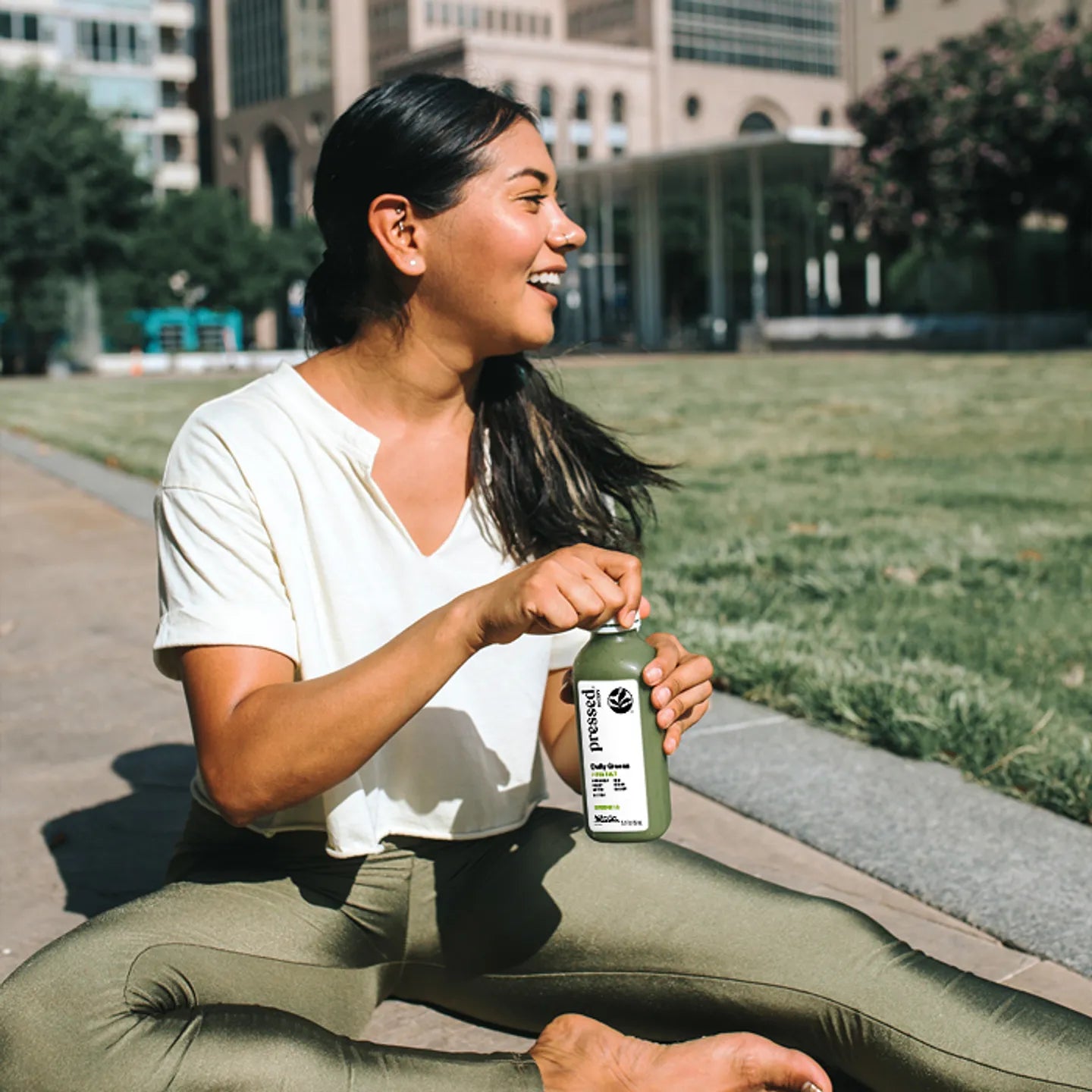 Woman sitting outdoors holding a green bottle with a cityscape in the background