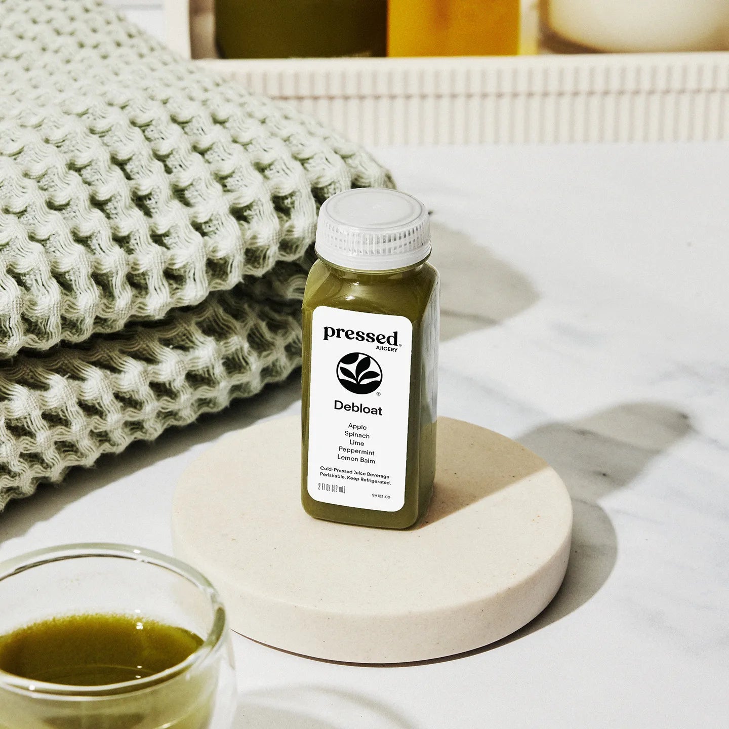 Bottle of 'pressed' Deboat supplement on a marble coaster with a glass of liquid next to it.
