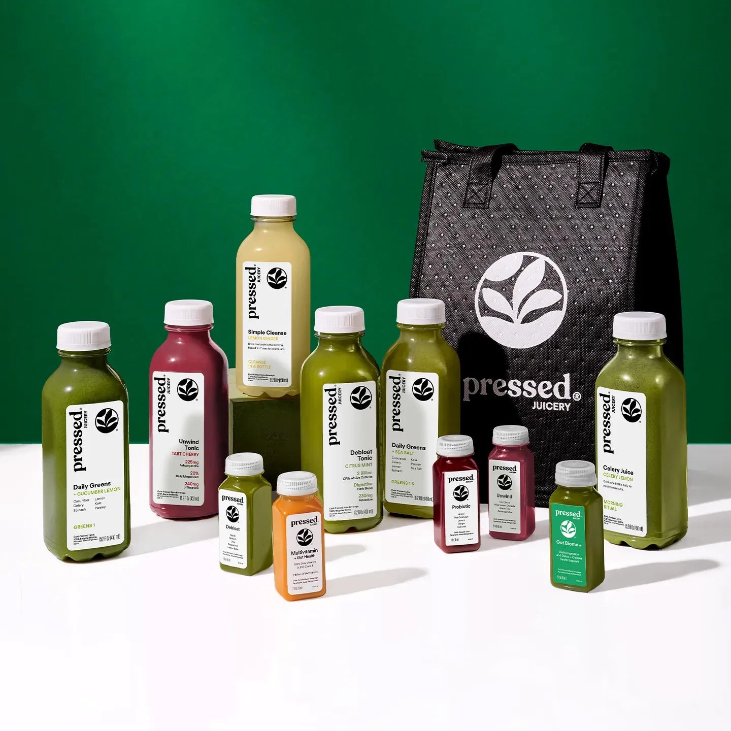 Collection of 'pressed' juice bottles and a black tote bag on a green background