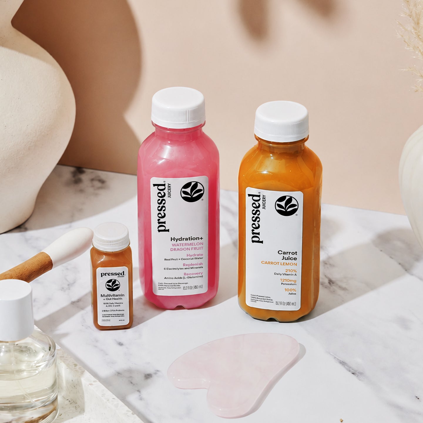 Pressed Juicery Skin Glow Beauty Pack featuring Carrot Juice, Hydration+ Watermelon Dragon Fruit, and Multivitamin + Gut Health shot in a beauty-inspired setting