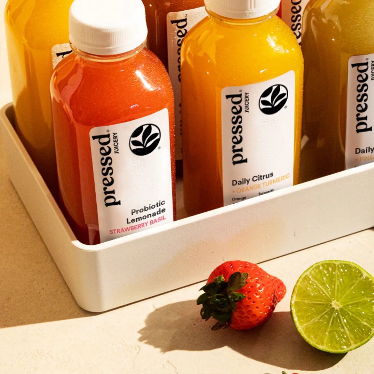 Bottles of 'pressed' juice with a strawberry and lime on a wooden surface