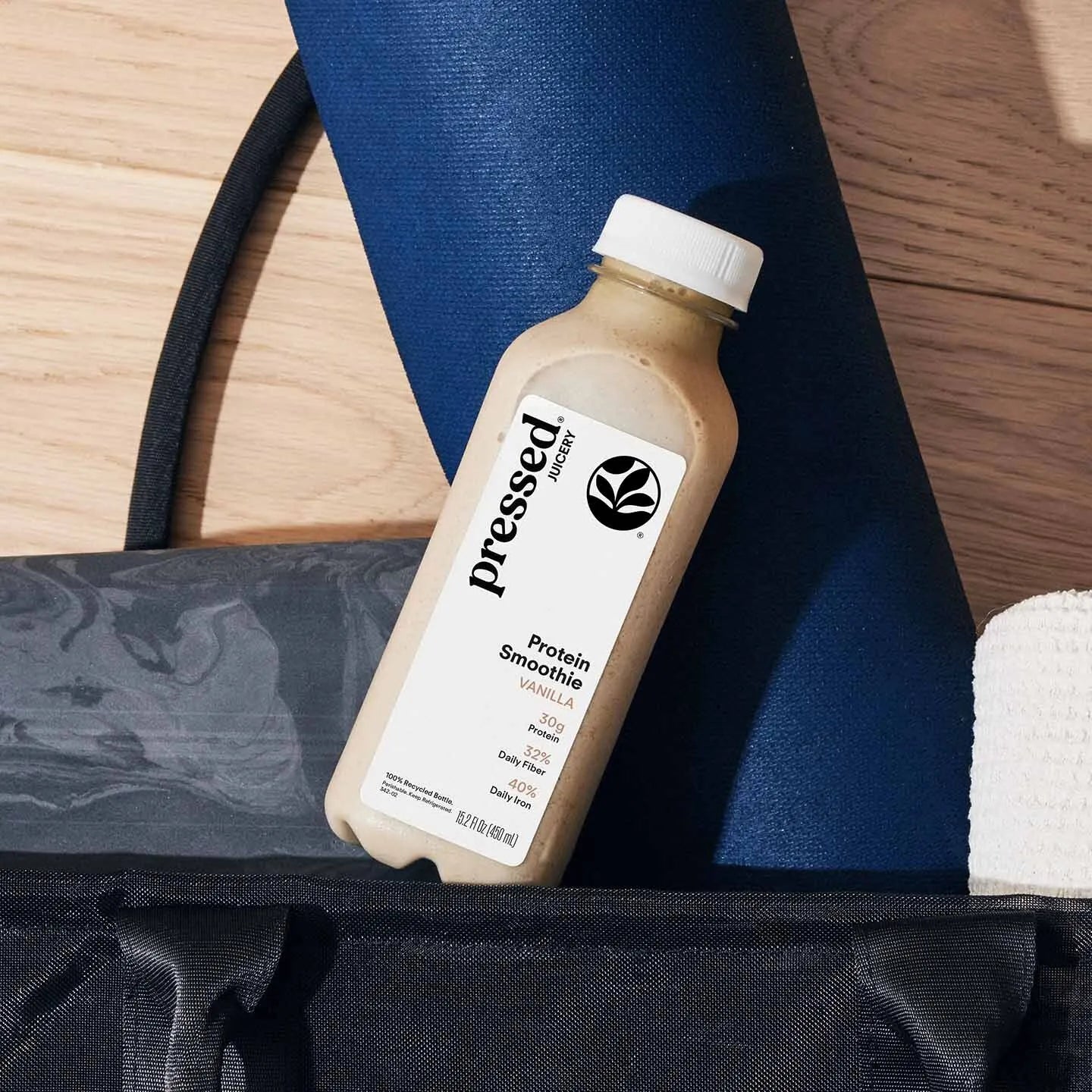 Pressed Protein Smoothie bottle on a wooden surface with a blue mat and black bag.