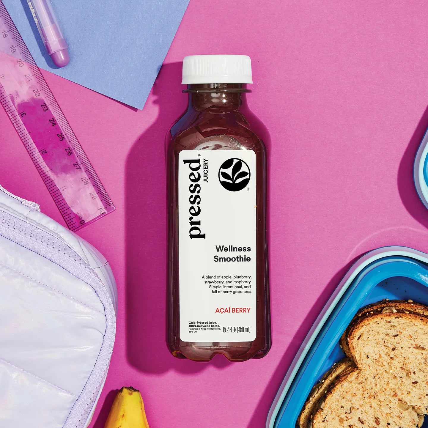 Bottle of pressed juicery Wellness Smoothie on a pink background with school supplies and food items.