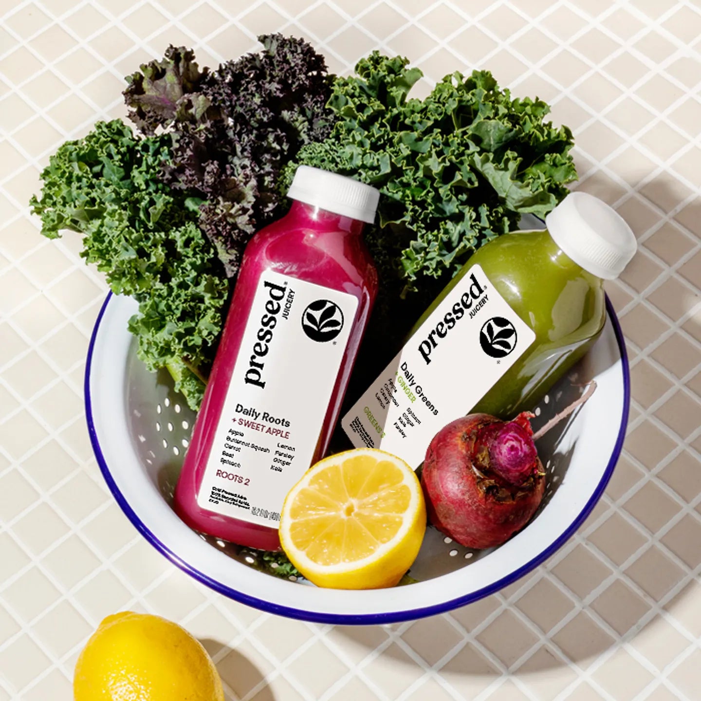 Two bottles of 'pressed' juice with greens and a lemon on a checkered tablecloth.