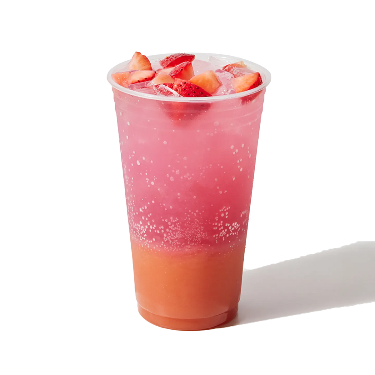 Pink and orange layered drink with strawberries in a clear cup on a white background