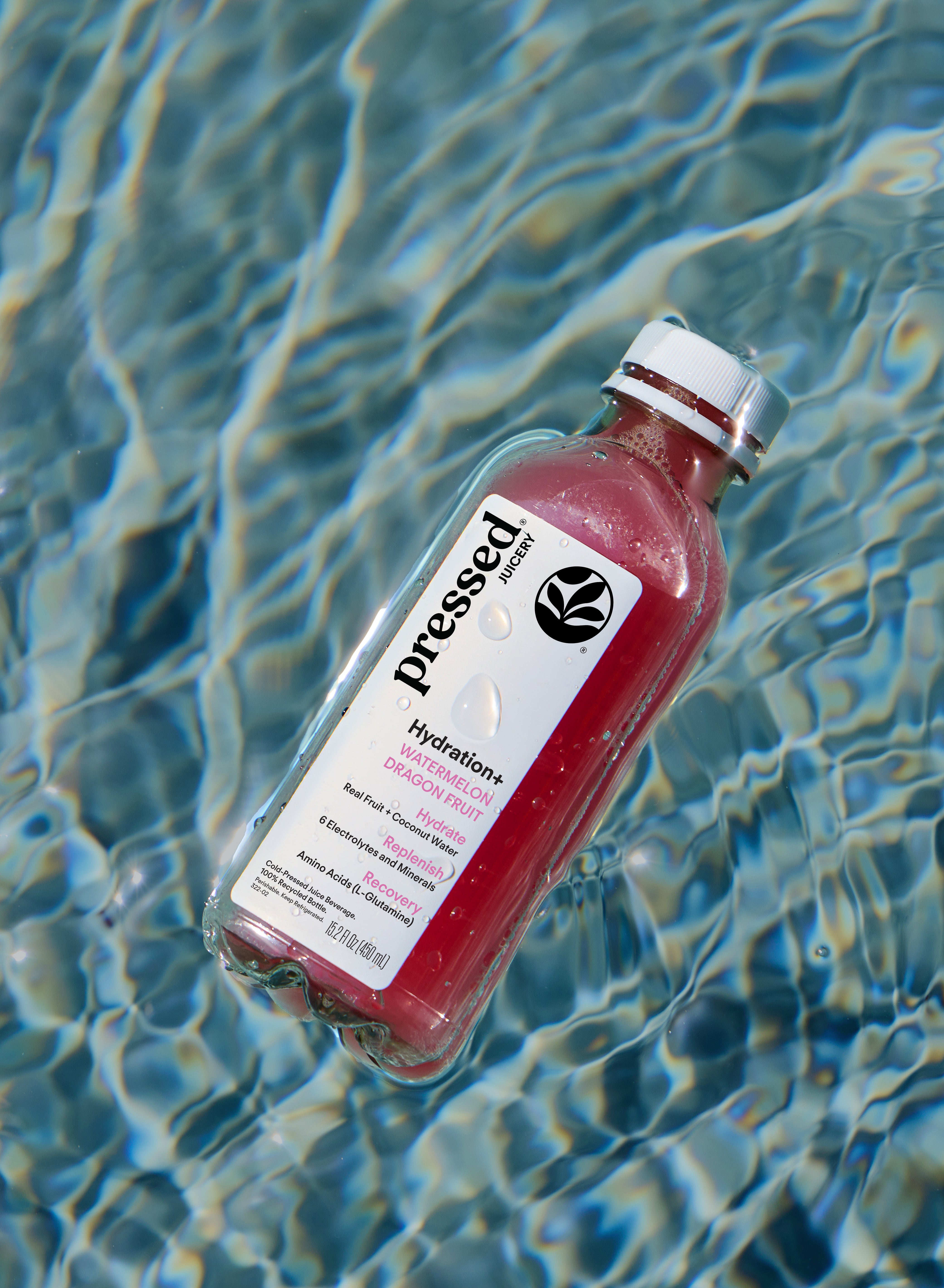 A bottle of Pressed Hydration+ sports drink in watermelon dragon fruit flavor, floating on rippling blue pool water.