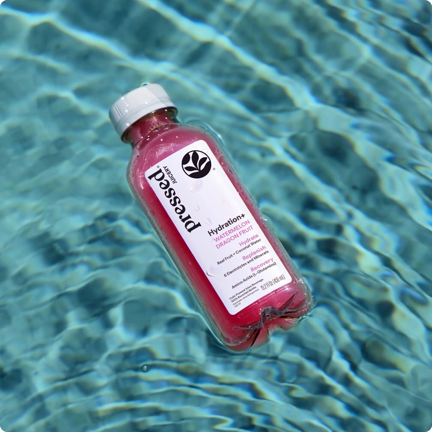 A bottle of Pressed Health Hydration+ Grapefruit Juice floating on rippling blue pool water.