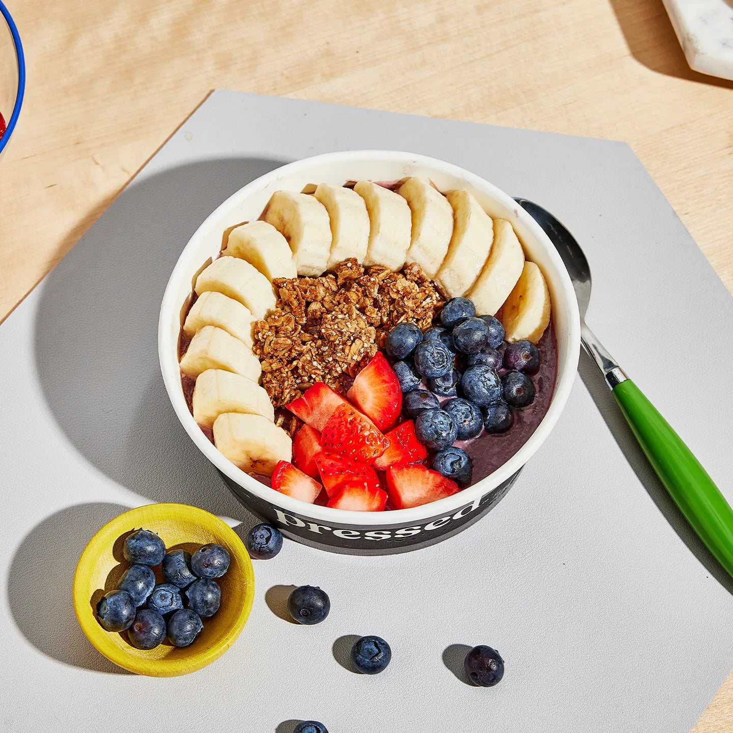 A bowl of acai bowl with bananas, strawberries, and blueberries on a gray surface.