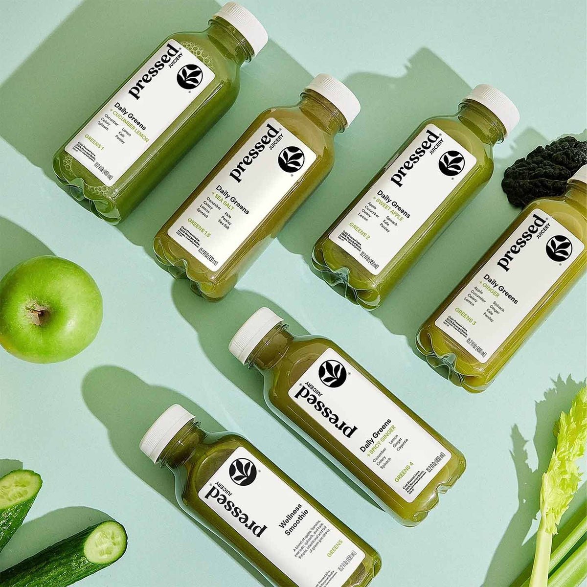 Bottles of 'pressed!' juice with green vegetables on a light green background