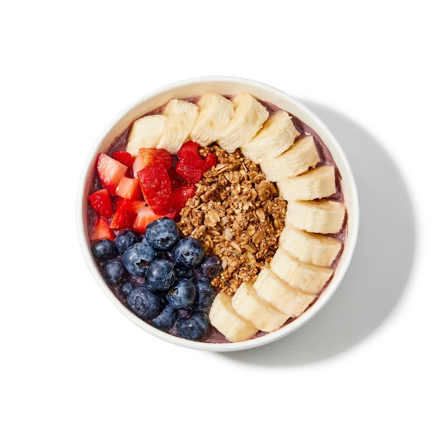 A bowl of acai bowl with bananas, strawberries, blueberries, and granola on a white background