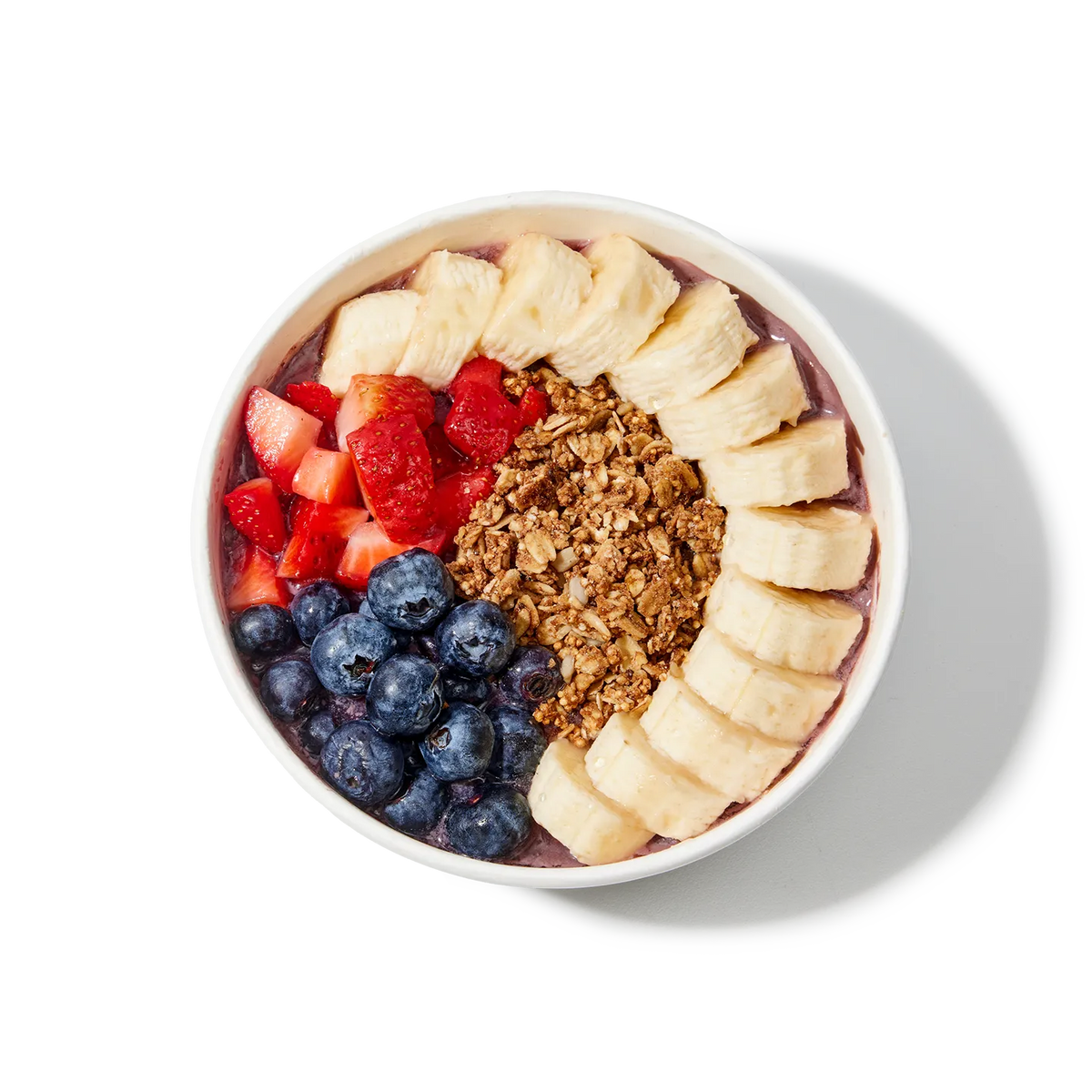 A bowl of acai bowl with bananas, strawberries, blueberries, and granola on a white background