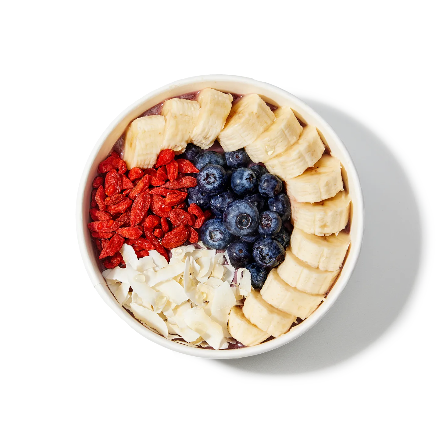Fruit bowl with bananas, blueberries, goji berries, and coconut flakes on a white background