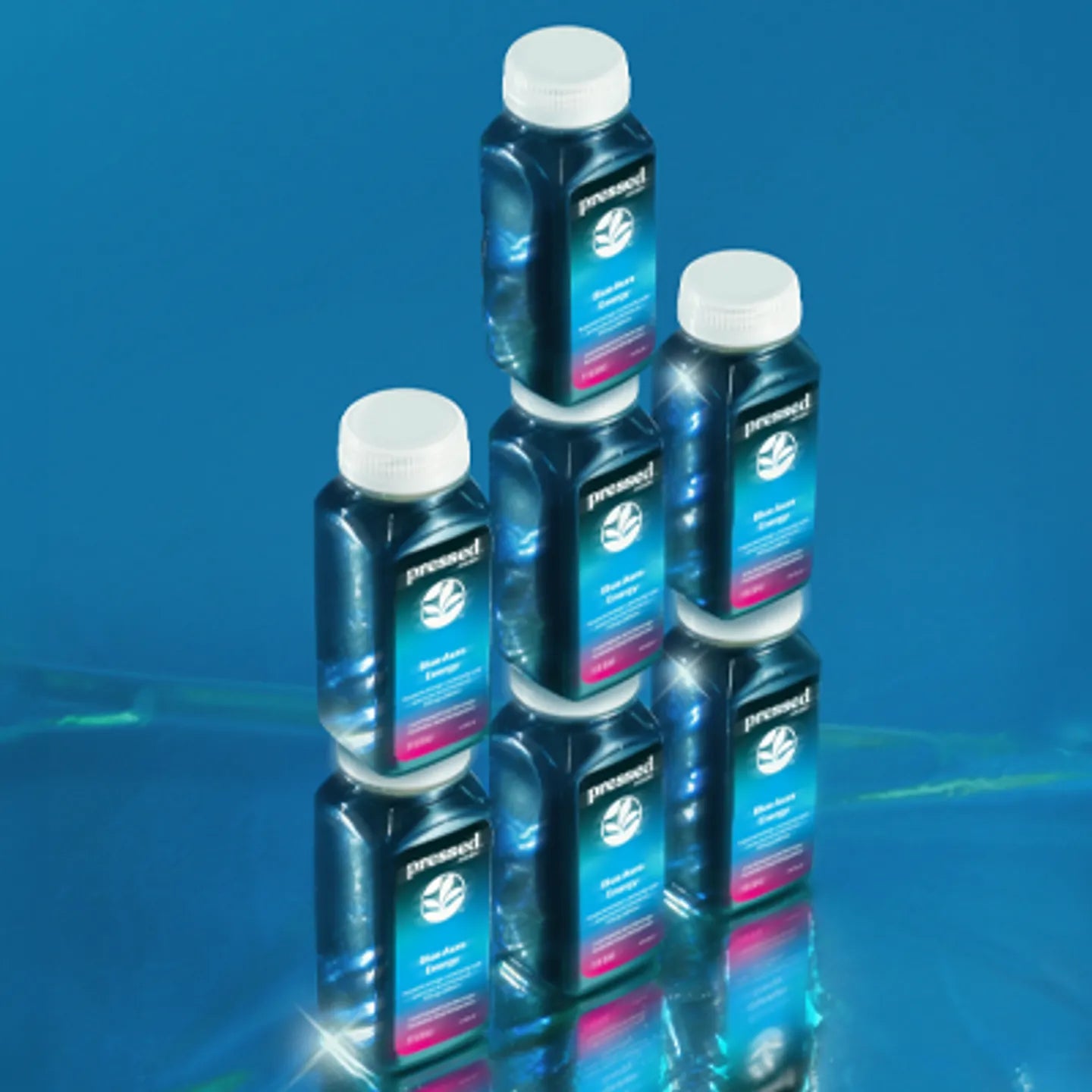 Stack of Blue Aura Energy Shot bottles on a reflective blue surface with a blue gradient background