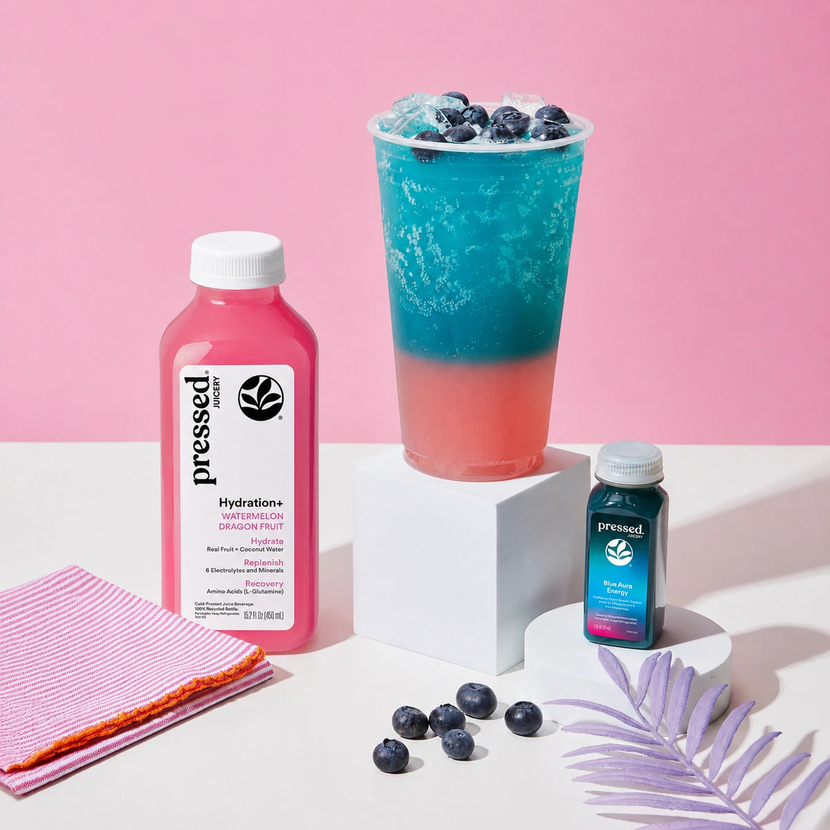 Two bottles of 'pressed' drinks with a colorful layered drink on a pink background