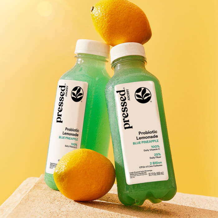 Two bottles of 'Pressed' Probiotic Lemonade with lemons on a yellow background