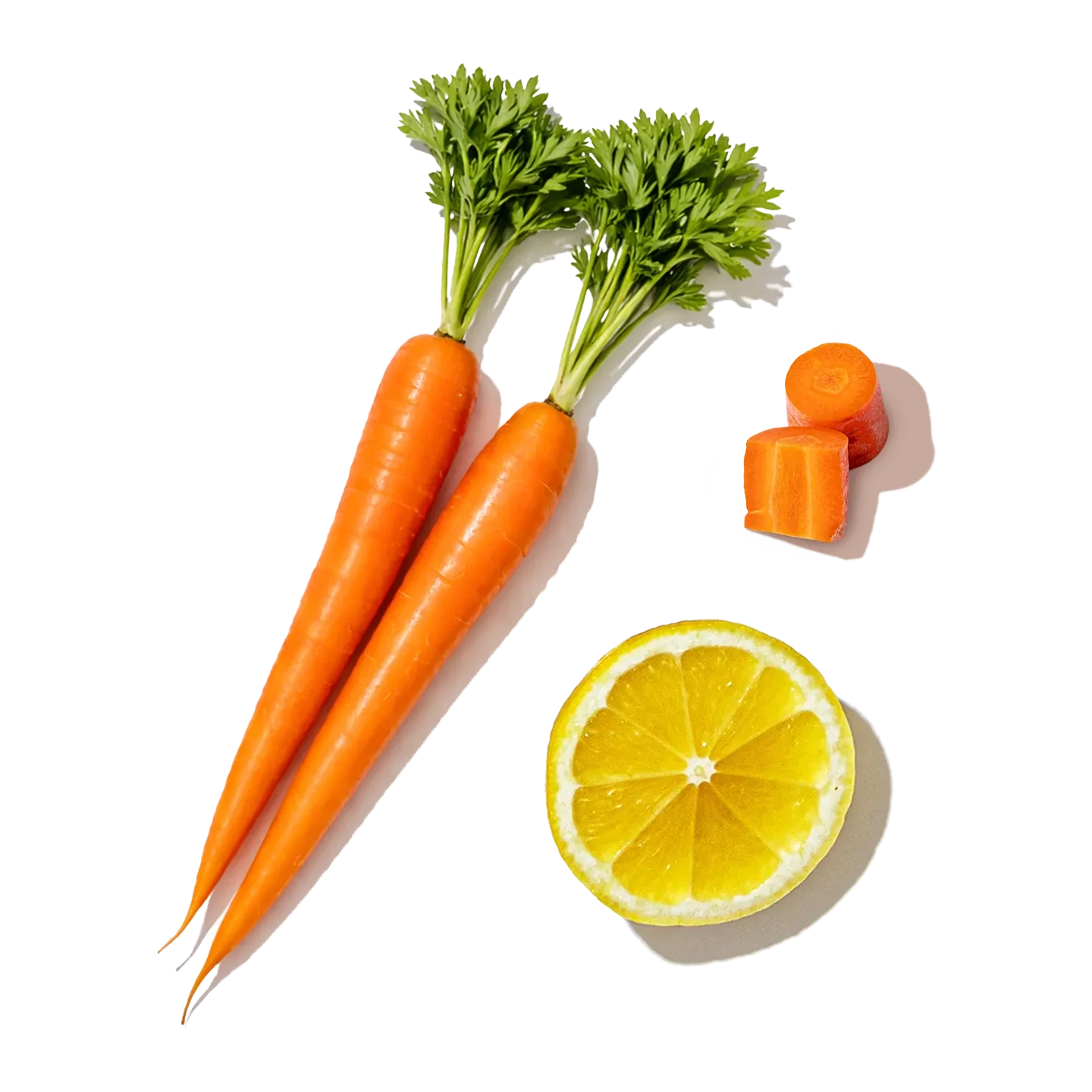 Three whole carrots with green tops, a sliced lemon, and small carrot pieces on a white background.