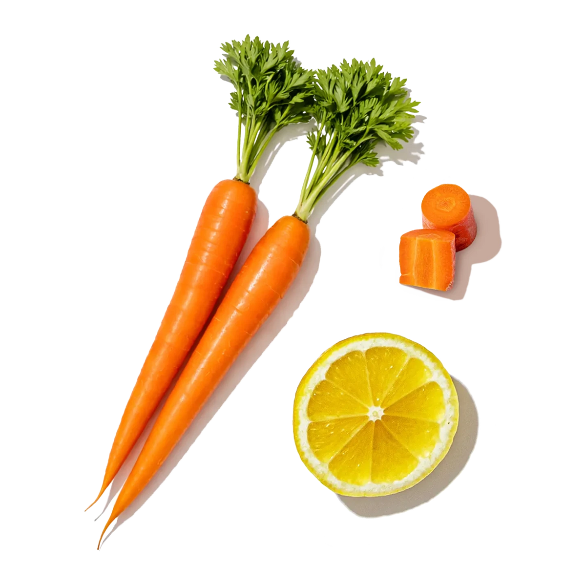 Three whole carrots with green tops, a sliced lemon, and small carrot pieces on a white background.