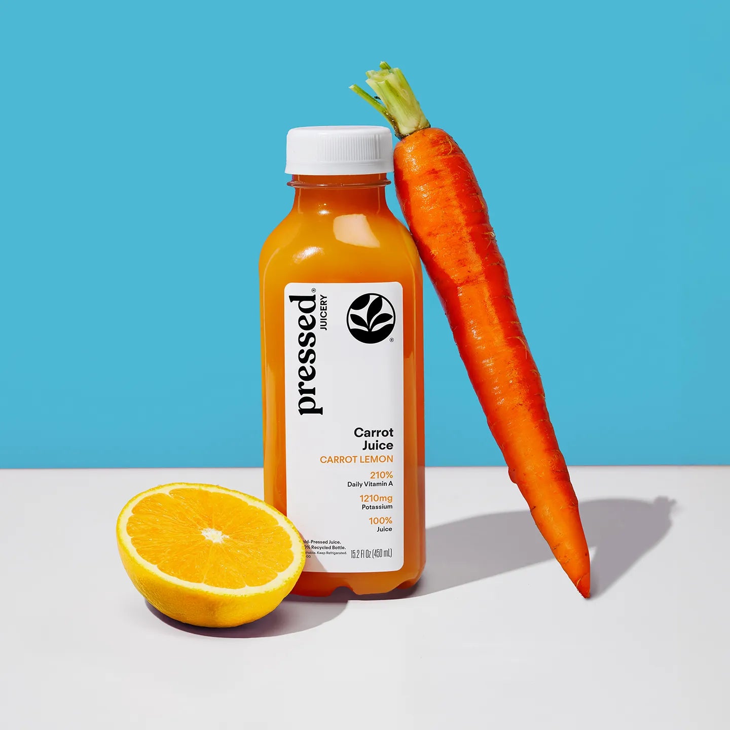 Bottle of pressed carrot juice with a carrot and half an orange on a blue background