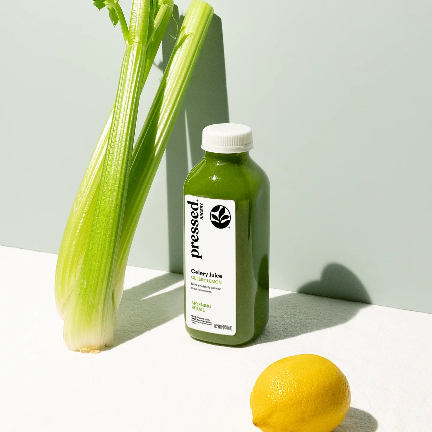 Bottle of 'pressed' celery juice with celery and a lemon on a light background