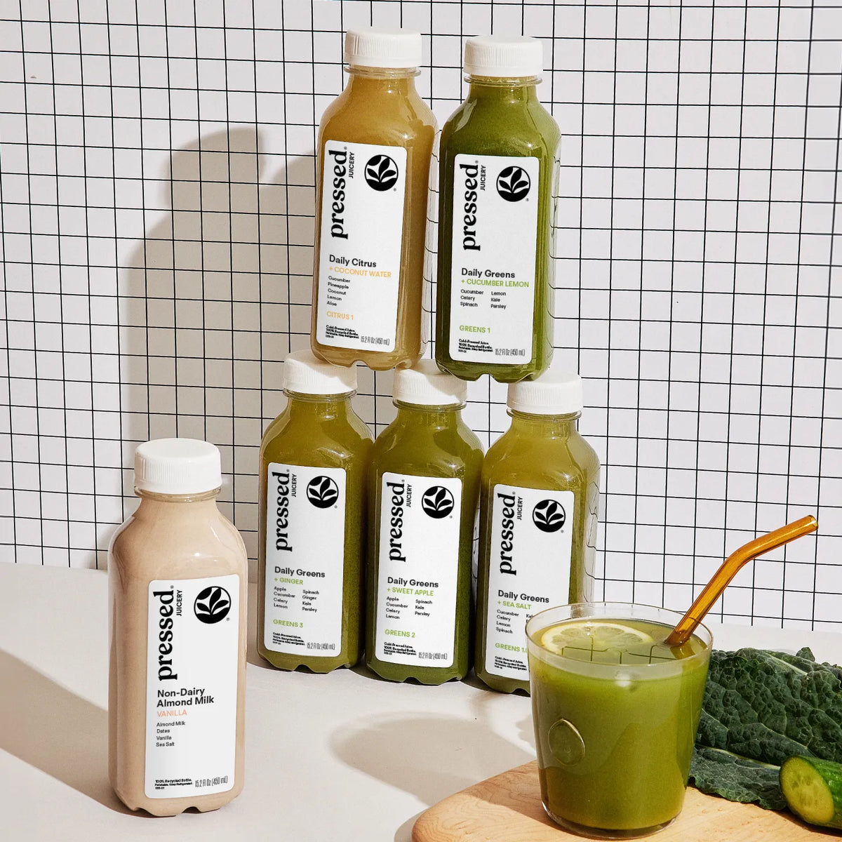 Bottles of 'pressed' brand juice on a checkered background with a glass of juice and ingredients.