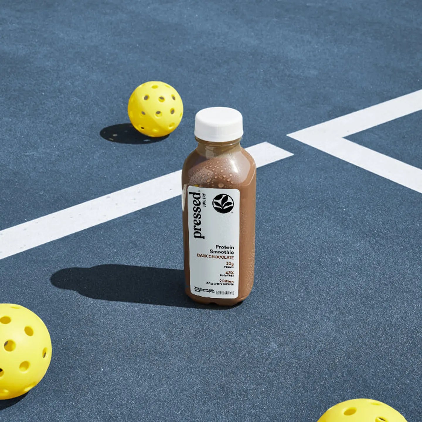 Bottle of 'pressed' protein shake on a blue court with yellow balls