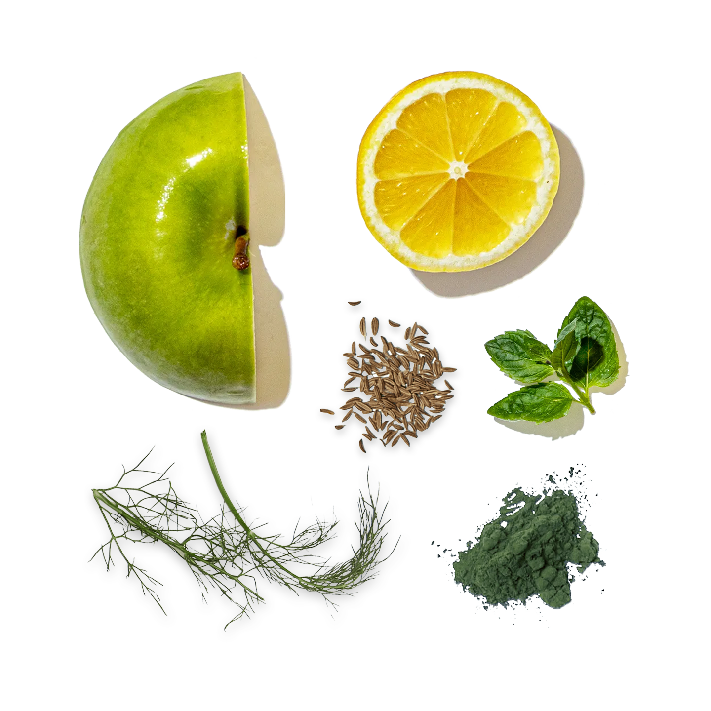Collection of green fruits and vegetables including an apple, lemon, lime, spinach, dill, and cumin seeds on a white background.