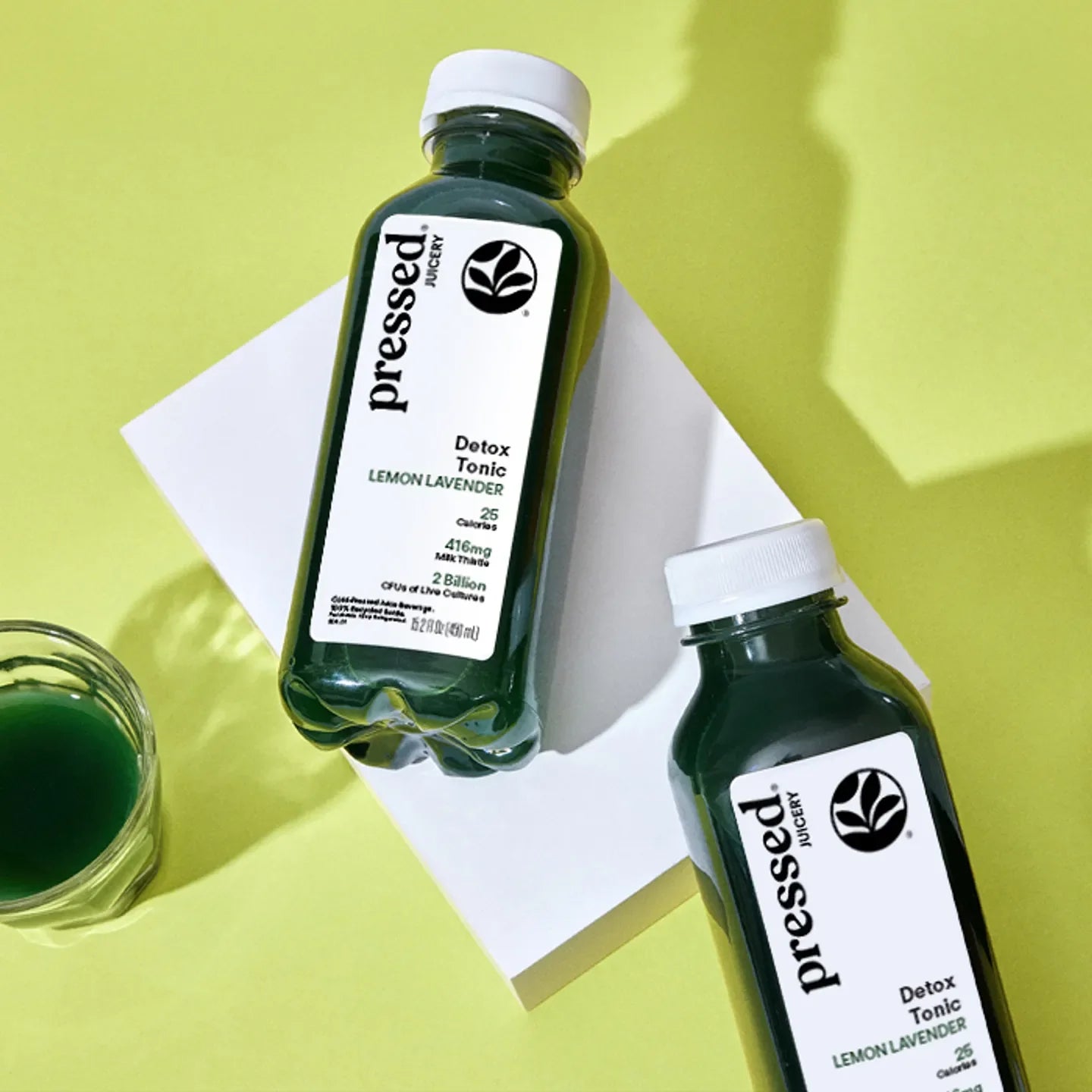 Two bottles of 'Pressed Juicery' Detox Tonic on a bright yellow background