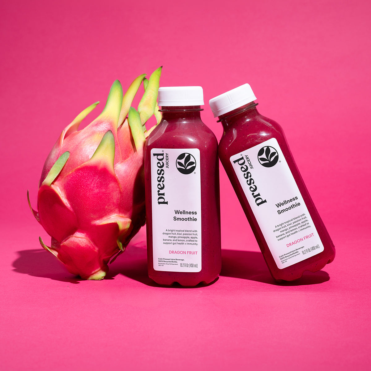 Pressed Juicery Dragon Fruit Wellness Smoothie bottles with fresh dragon fruit on a pink background