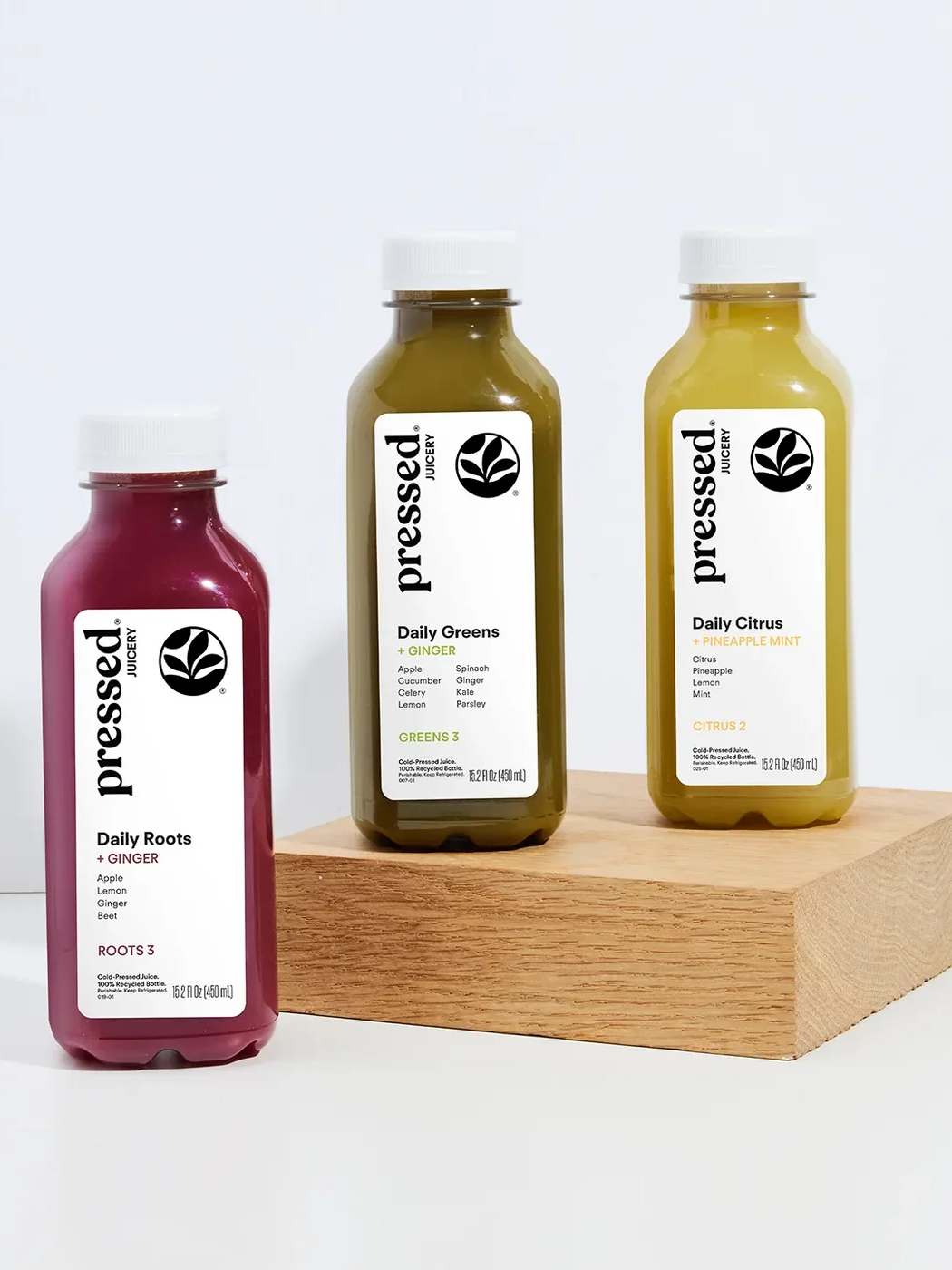 Pressed Juicery Roots 3, Greens 3 and Citrus 2 cold-pressed juice bottles arranged around a wooden display block.