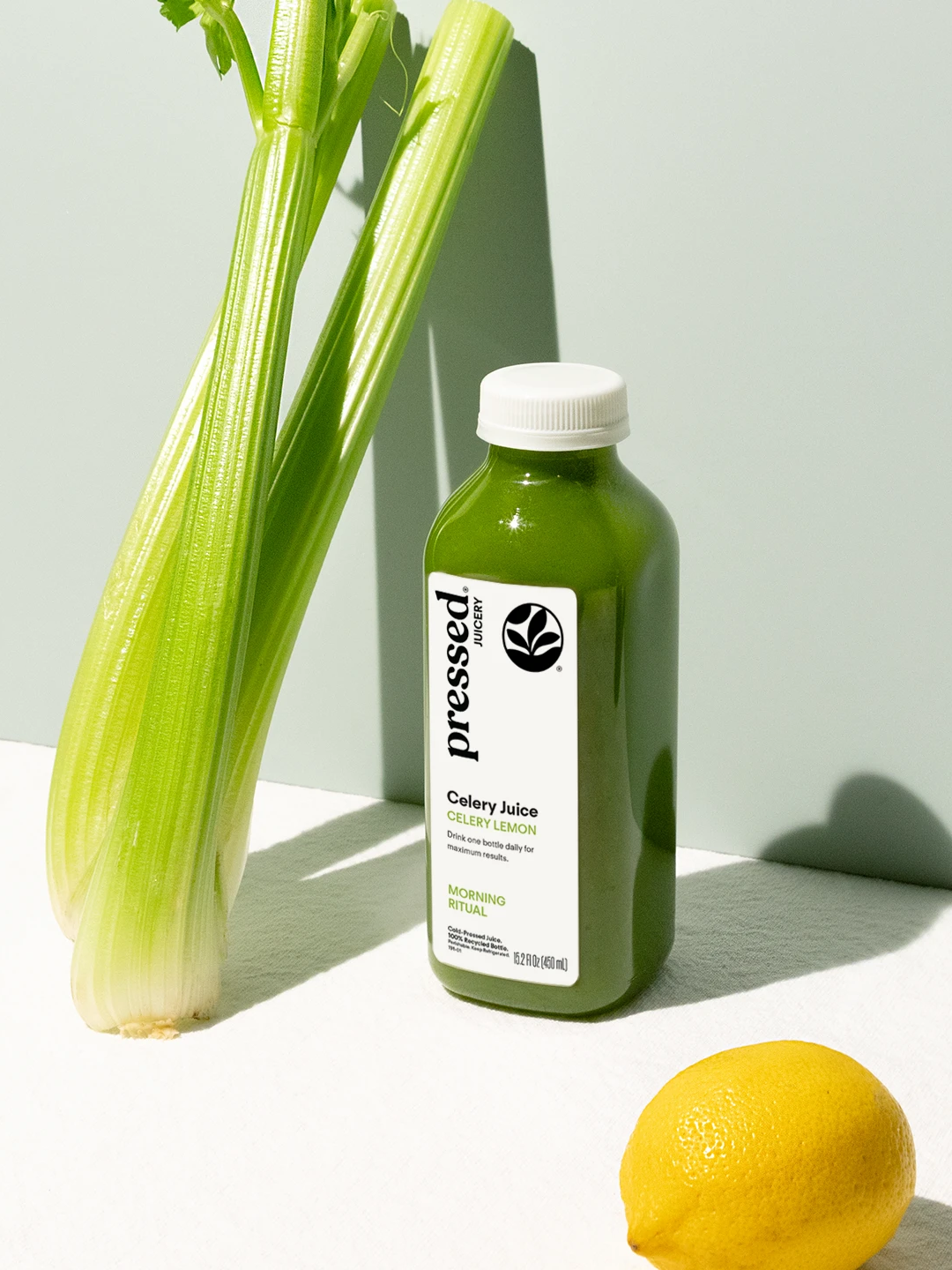 Pressed Juicery cold-pressed celery juice bottle with fresh celery stalks and a lemon.
