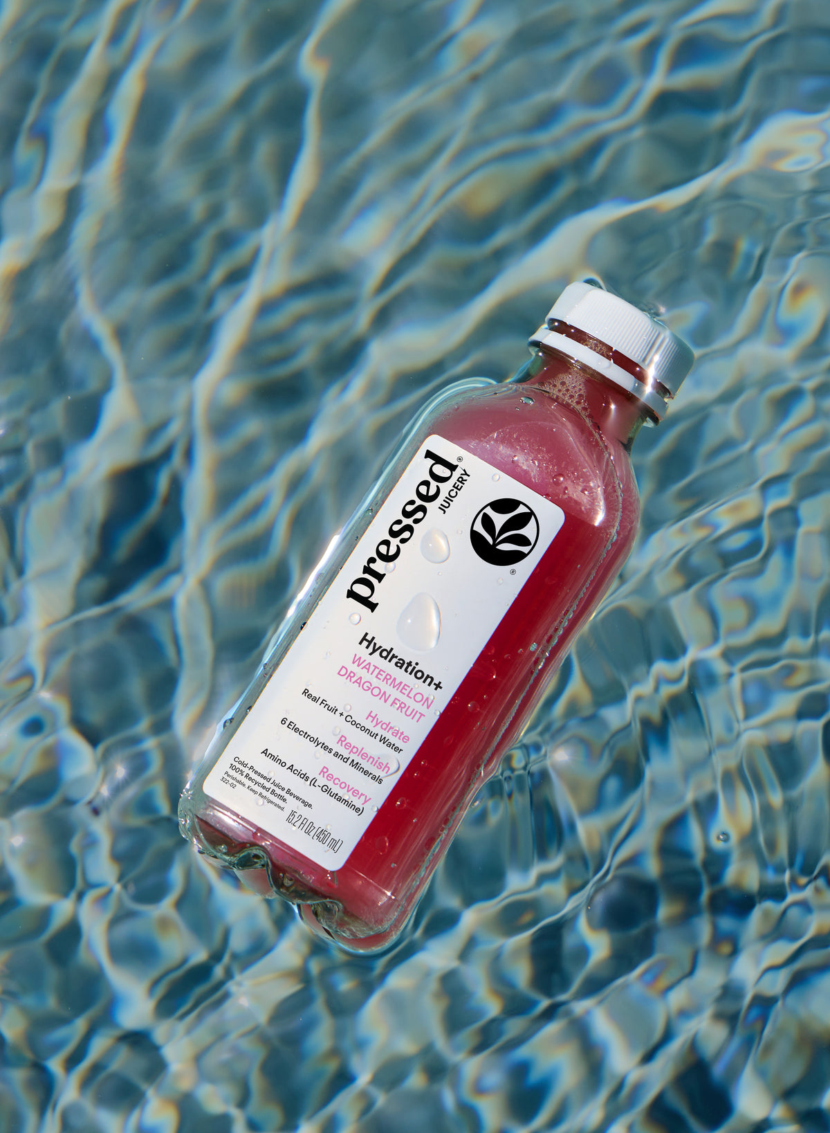 A bottle of Pressed Hydration+ sports drink in watermelon dragon fruit flavor, floating on rippling blue pool water.