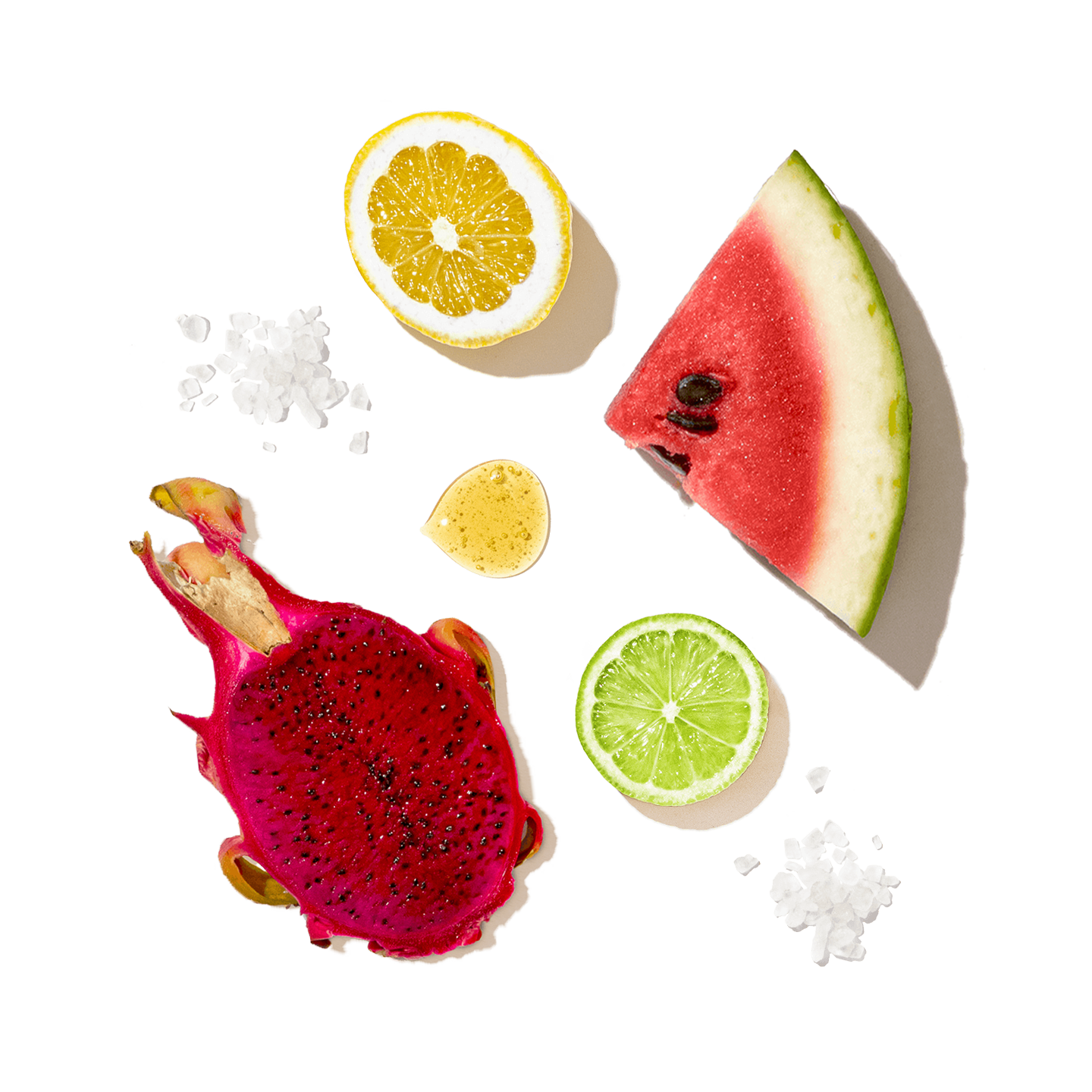 A styled flat-lay of fresh fruits on a white background, including a slice of watermelon, a halved dragon fruit, a halved orange, a lime slice, and a small yellow fruit piece, with scattered coarse salt crystals.