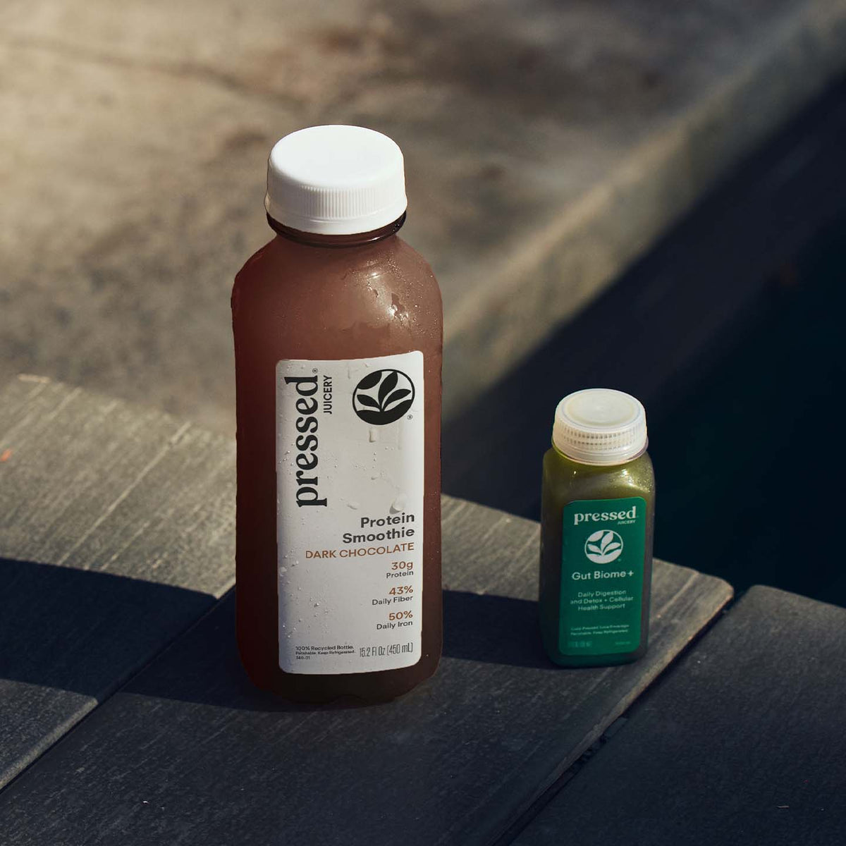 Pressed Juicery Dark Chocolate Protein Smoothie and Gut Biome+ Shot on a wooden table in sunlight.