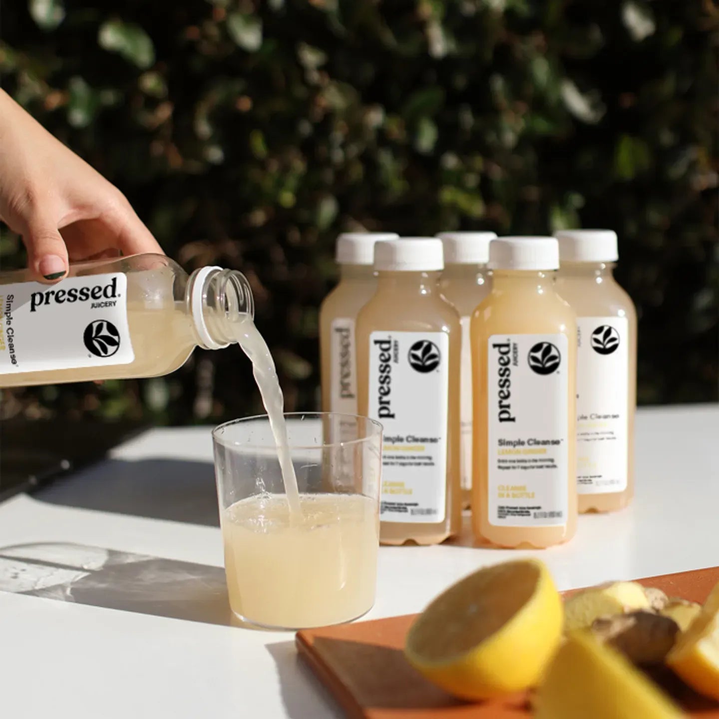Person pouring 'pressed' lemonade into a glass with lemon and apple on a table.
