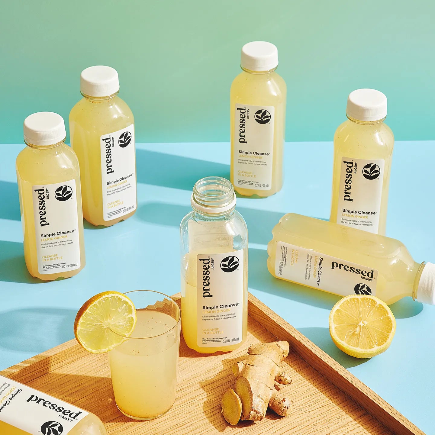 Bottles of 'Pressed'Simple Cleanser on a blue and green gradient background with lemons and ginger.