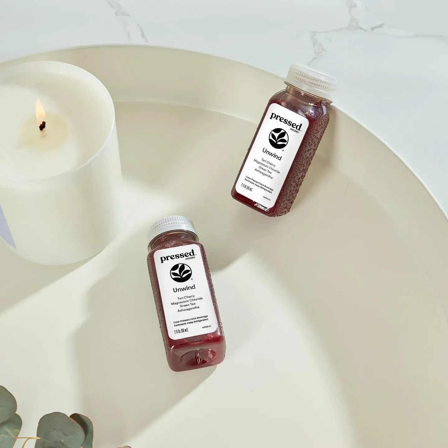 Two 'pressed' Calm products on a white surface with a candle in the background