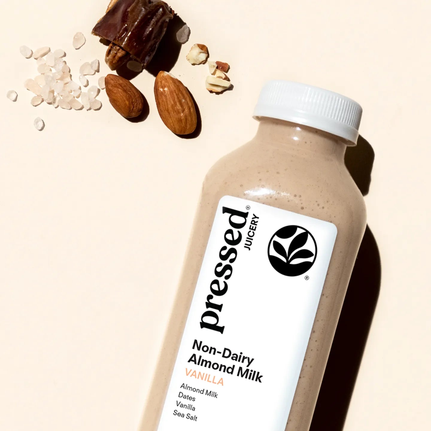 Bottle of pressed juicery Non-Dairy Almond Milk Vanilla with almonds and dates on a beige background