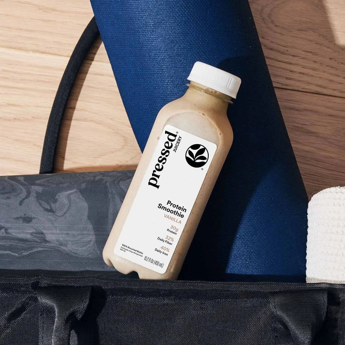 Pressed Protein Smoothie bottle on a wooden surface with a blue mat and black bag.
