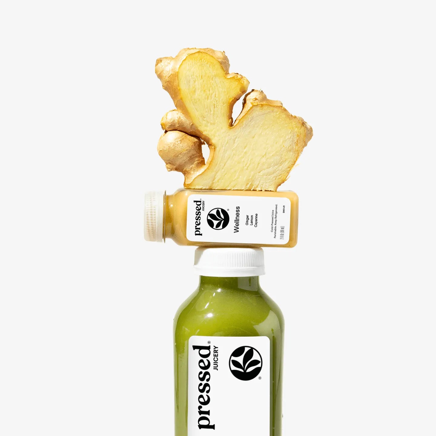 Bottle of pressed Wellness juice with a piece of ginger on top against a white background