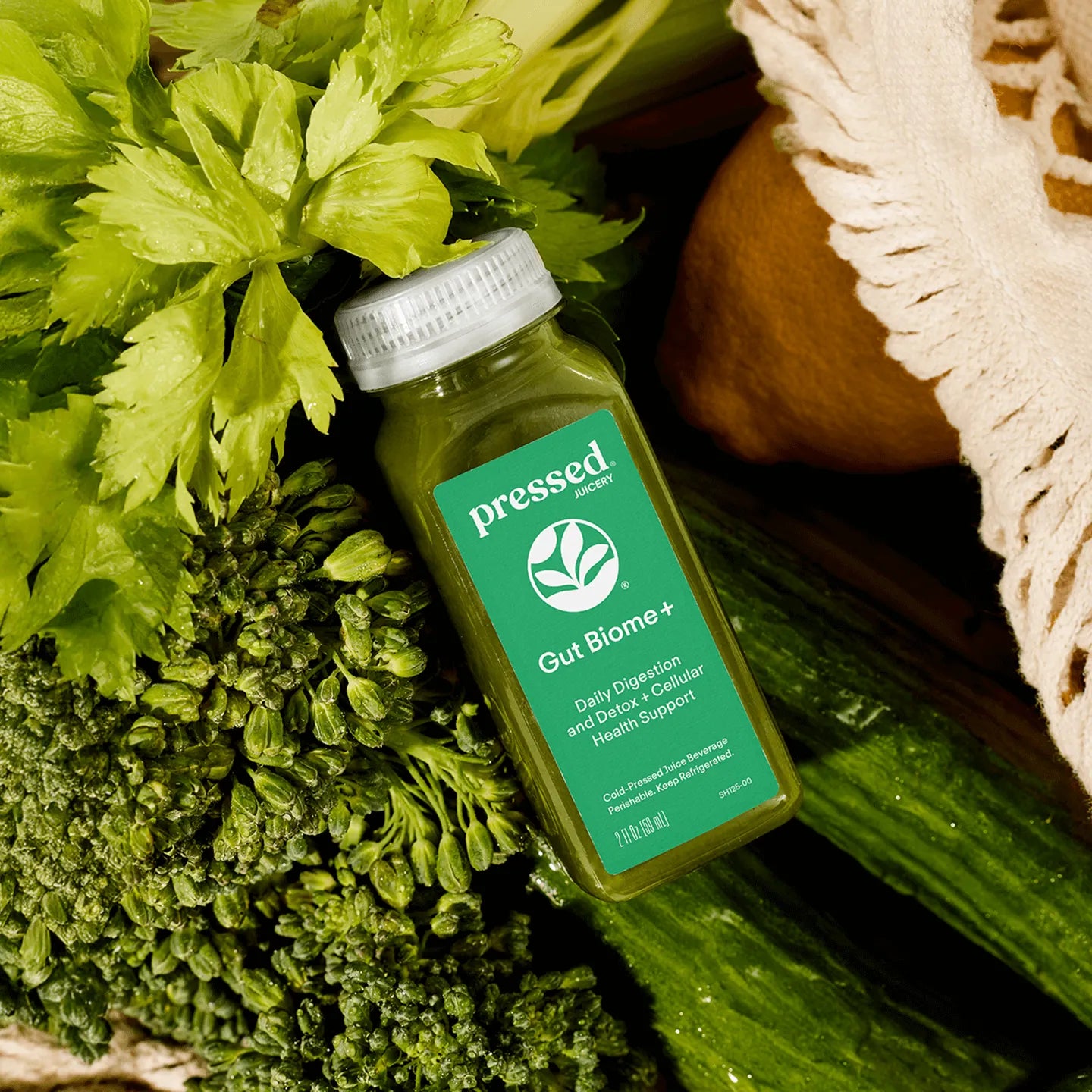 Bottle of 'Pressed' Gut Biome+ supplement surrounded by green vegetables on a wooden surface.